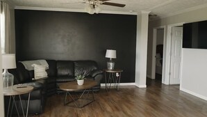 Uma sala de estar com um sofá de couro preto, uma mesa de centro de madeira e um ventilador de teto.