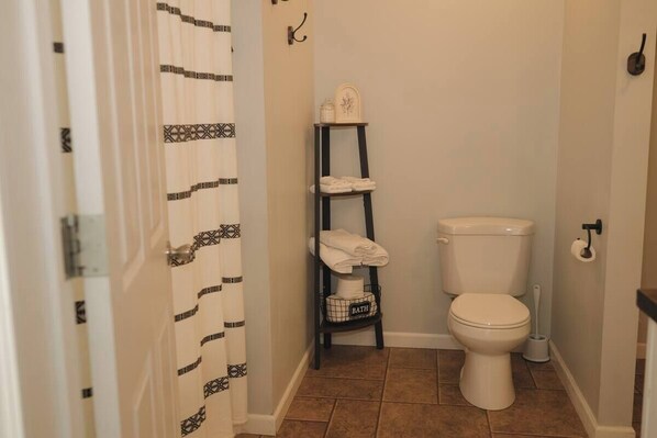 Une salle de bain avec des toilettes, une étagère avec des serviettes et un rideau de douche à motifs.