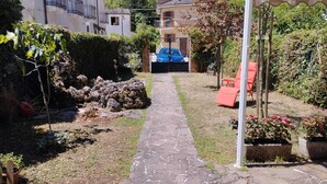 Un chemin de pierres mène à une maison devant laquelle est garée une voiture bleue, dans l’allée.