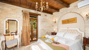 A bedroom with a stone wall, a wooden ceiling, a bed with white bedding, a bedside table, a mirror, and a chandelier.