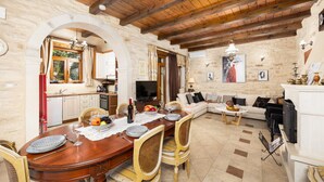 A spacious living area with a wooden dining table, chairs, and a sofa. There is a kitchen area with a red refrigerator and cabinets.
