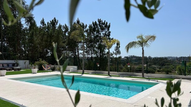 A rectangular swimming pool with a tiled deck, surrounded by a fence and trees.