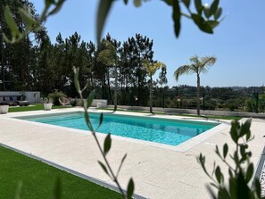 A rectangular swimming pool with a tiled deck, surrounded by a fence and trees. - Quinta las Laranjeiras (Leiria)