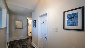 A hallway with wooden flooring, white walls, and framed artwork. - Adorable 2bd/2ba Home w/ Yard in Gentilly (New Orleans)
