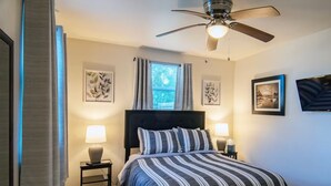 A bedroom with a bed, two bedside tables, a ceiling fan, and framed artwork on the walls. - Adorable 2bd/2ba Home w/ Yard in Gentilly (New Orleans)