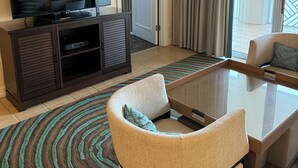 A hotel room with a TV on a cabinet, a sofa, a glass coffee table, and a view of the outdoors. - Best Amenities Resort- Bonita Spring, FL- 2BD/2BA (Bonita Springs)