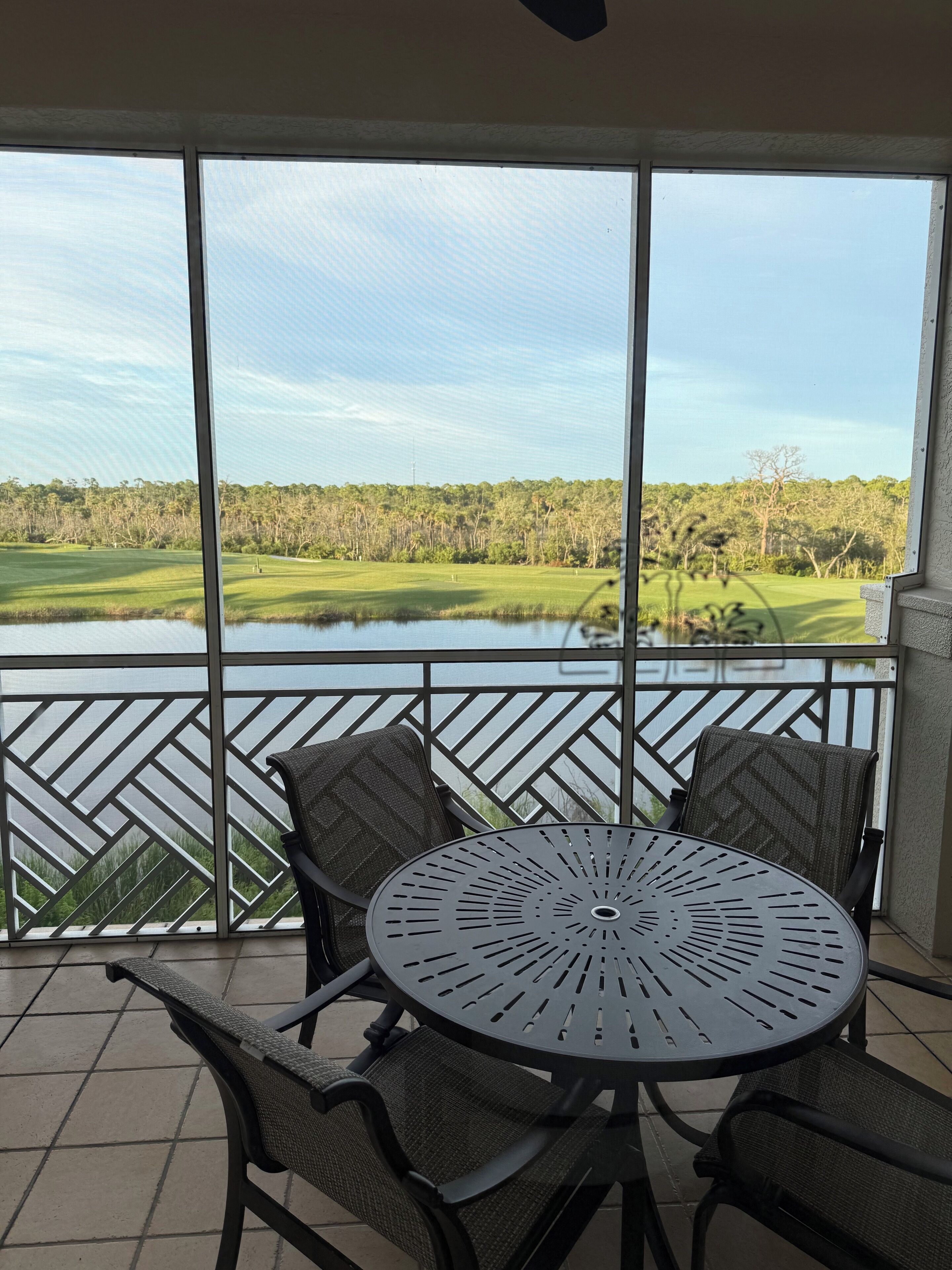 Un balcon avec une table et des chaises, donnant sur un terrain de golf et une zone boisée.