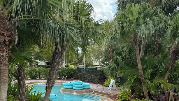 A pool area with a rope net, palm trees, and inflatable rings. - Best Amenities Resort- Bonita Spring, FL- 2BD/2BA (Bonita Springs)
