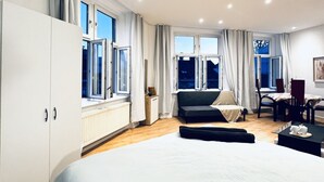 A modern bedroom with a large bed, a sofa, a dining table, and a window with curtains.
