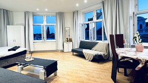 A modern hotel room with a bed, sofa, dining table, and large windows.