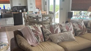 Un salón amplio con un sofá grande, una zona de comedor con mesa y sillas, una cocina con armarios blancos, y un balcón con vistas.