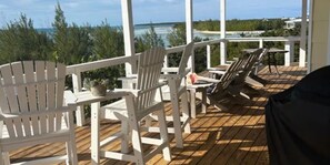 Een houten terras met witte Adirondack-stoelen en een tafel, met uitzicht op een strand en oceaan.
