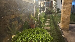 Un espacio exterior bien iluminado con muros de piedra, plantas en macetas y un pequeño jardín.