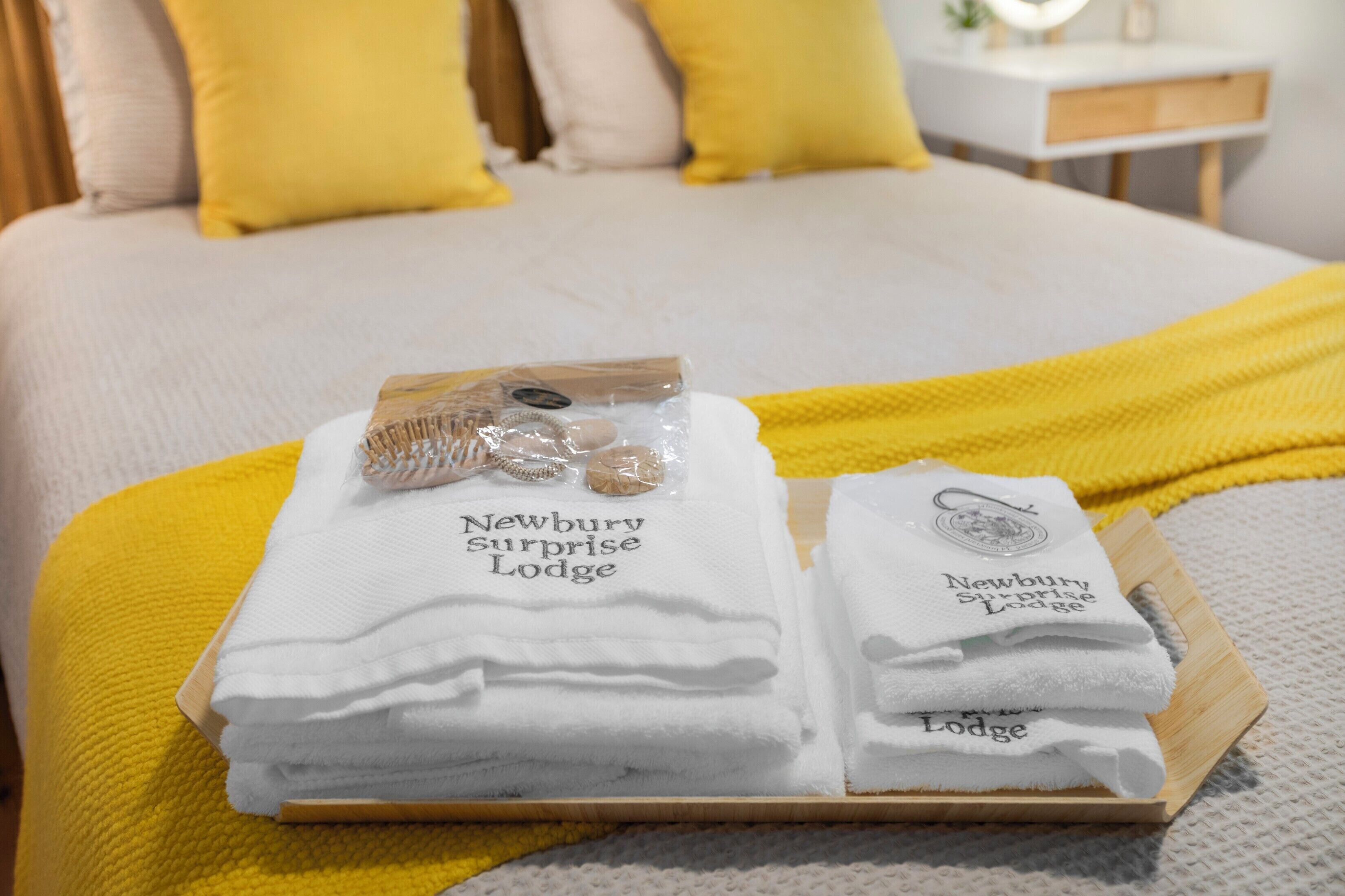 Una cama bien hecha con un edredón amarillo, una bandeja con toallas dobladas y un pequeño set de artículos de aseo.
