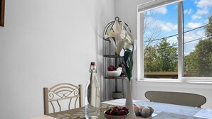 Un coin repas avec une table dressée pour deux personnes, un vase rempli de lys blancs, une bouteille et un saladier de fruits.