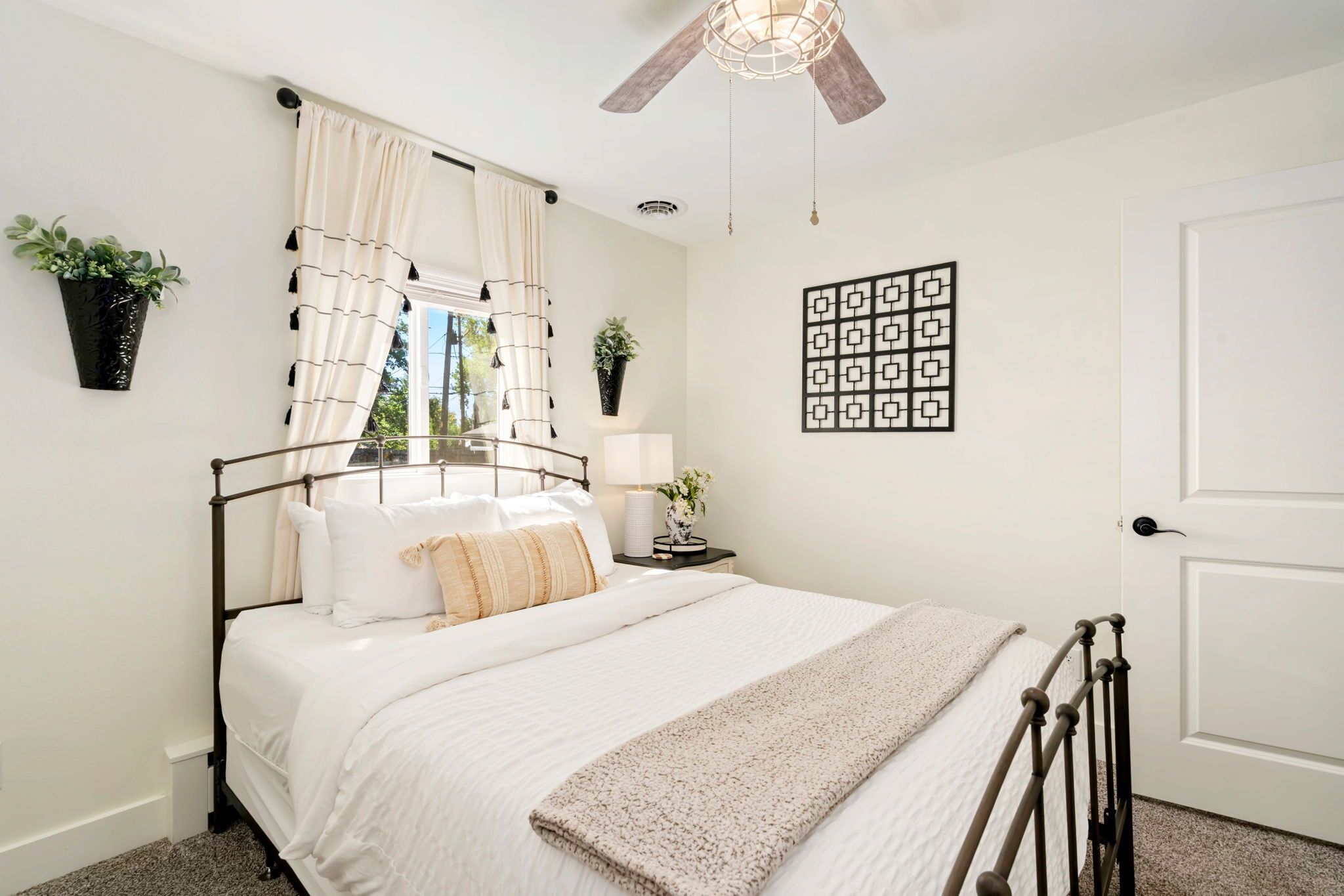 Une chambre à coucher bien aménagée, avec un lit, des tables de chevet, un ventilateur de plafond et des jardinières fixées au mur.