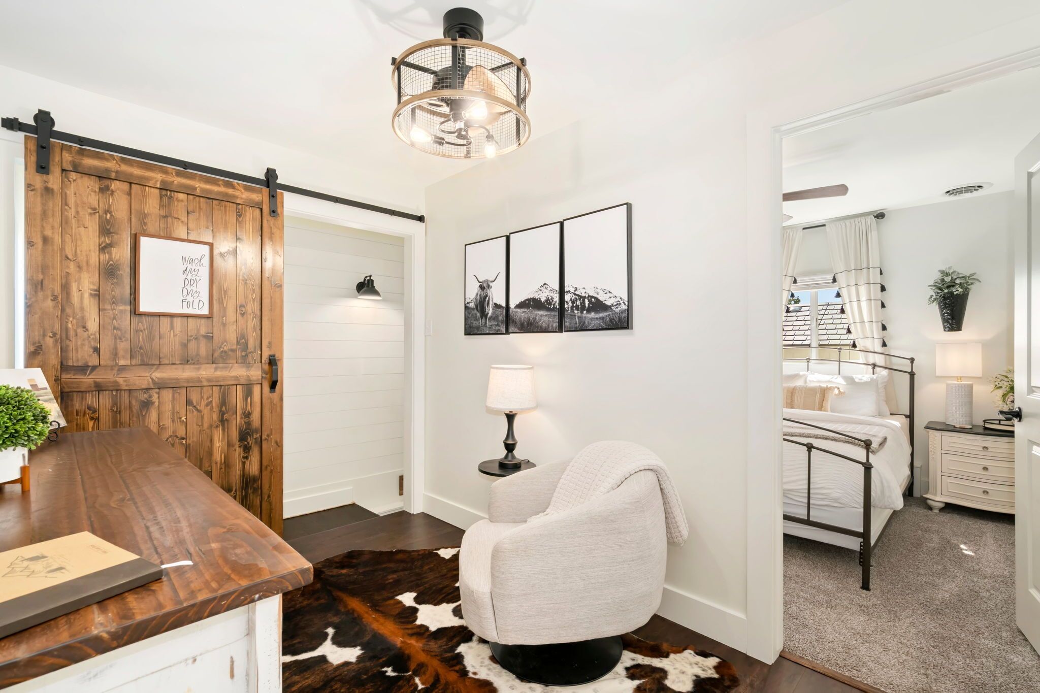 A modern interior with a wooden sliding door, a cowhide rug, a framed picture, a lamp, and a bed with a white headboard.