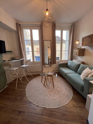 Ein modernes Wohnzimmer mit einem runden Glastisch, einem grünen Sofa und Holzboden.
