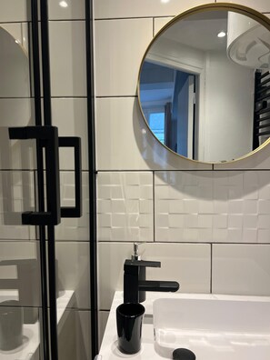 Ein modernes Badezimmer mit einer Duschkabine aus Glas, einem schwarzen Wasserhahn und einem runden Spiegel an der Wand.