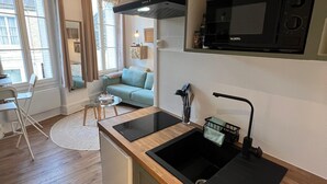 Una cocina compacta con microondas integrado, un lavamanos y un refrigerador pequeño. La cocina está conectada a una sala de estar con un sofá y una mesa de comedor.