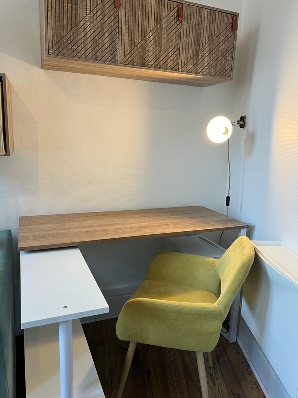 Un espacio de trabajo con un escritorio de madera, una silla amarilla, una mesita auxiliar blanca y una lámpara de pared.