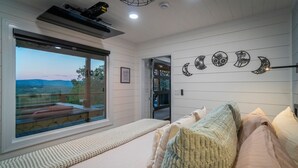 Une chambre avec une grande fenêtre, un lit garni de nombreux oreillers et un mur décoré de motifs représentant les différentes phases de la lune.