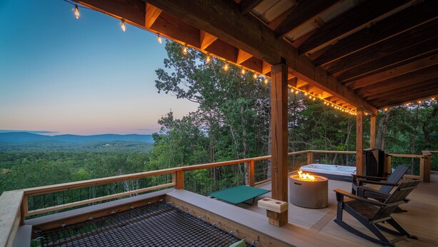 Une terrasse en bois avec un jacuzzi, des sièges d’extérieur et une vue sur la forêt.