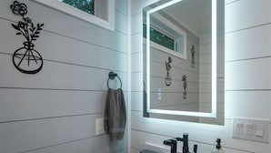 Une salle de bain moderne avec un lavabo blanc, un robinet noir et un miroir doté d’un éclairage intégré.