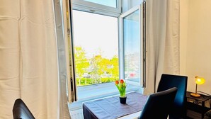 Una habitación con una mesa, sillas, un ventanal con cortinas y una lámpara.