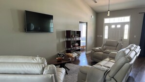 A modern living room with a large flat-screen TV, a beige sofa, a recliner, and a bookshelf. - Sunny Daze lake time is always a great time! (Lake Placid)
