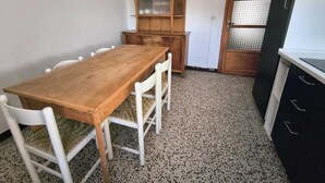A small, compact kitchen with a wooden table and chairs, a wooden cabinet with a glass door, and a refrigerator. - BLACK DOLOMYTE Apartment (Schilpario)