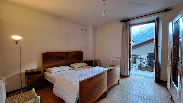A bedroom with a wooden bed, a nightstand, a lamp, and a view of a snowy mountain through a sliding door. - BLACK DOLOMYTE Apartment (Schilpario)