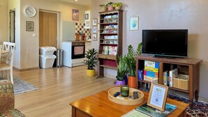A living room with a wooden coffee table, a television, a bookshelf, and a kitchen area in the background.