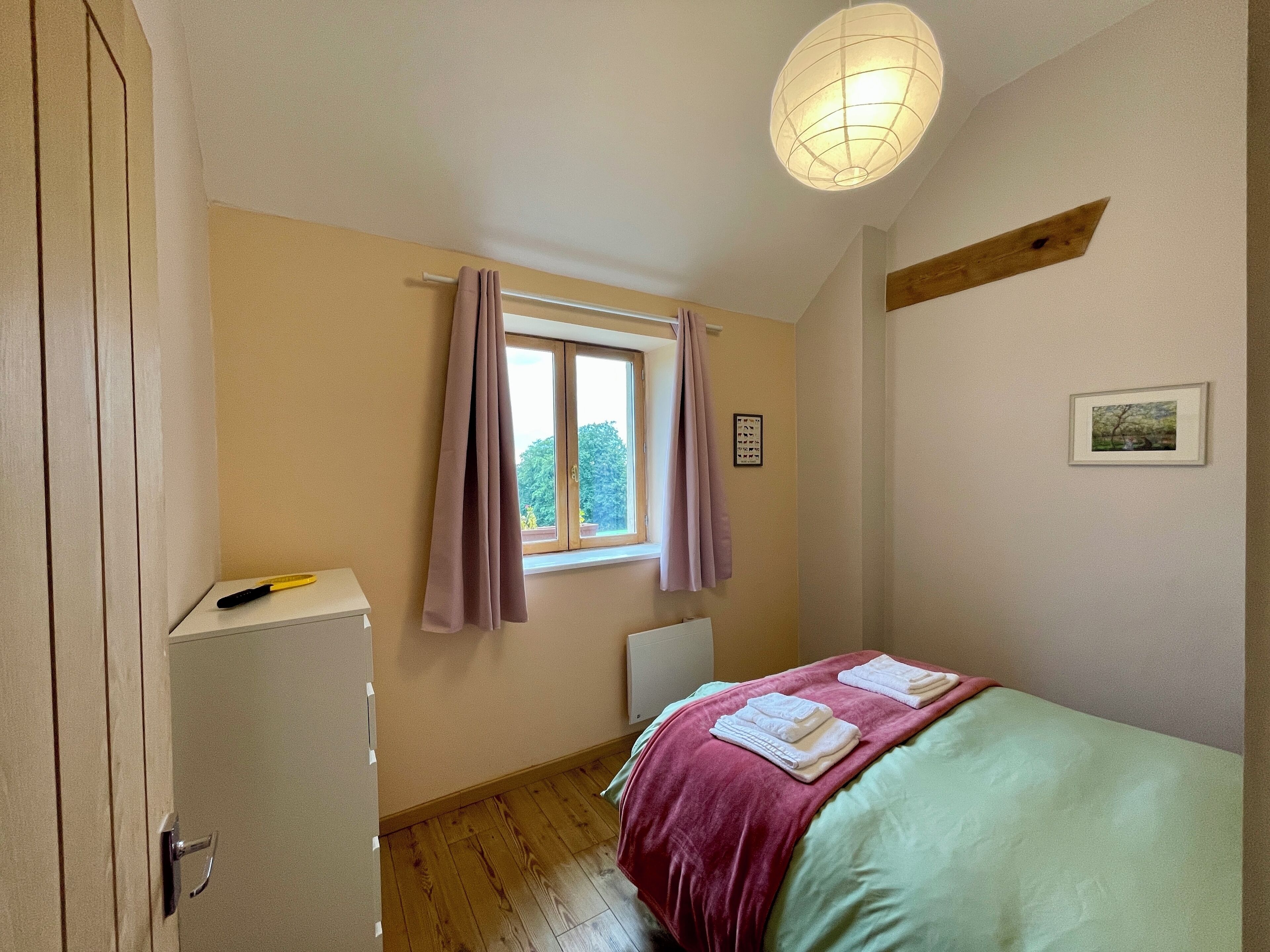 Una camera da letto con un letto, una finestra con tende, un termosifone e un quadro appeso al muro.