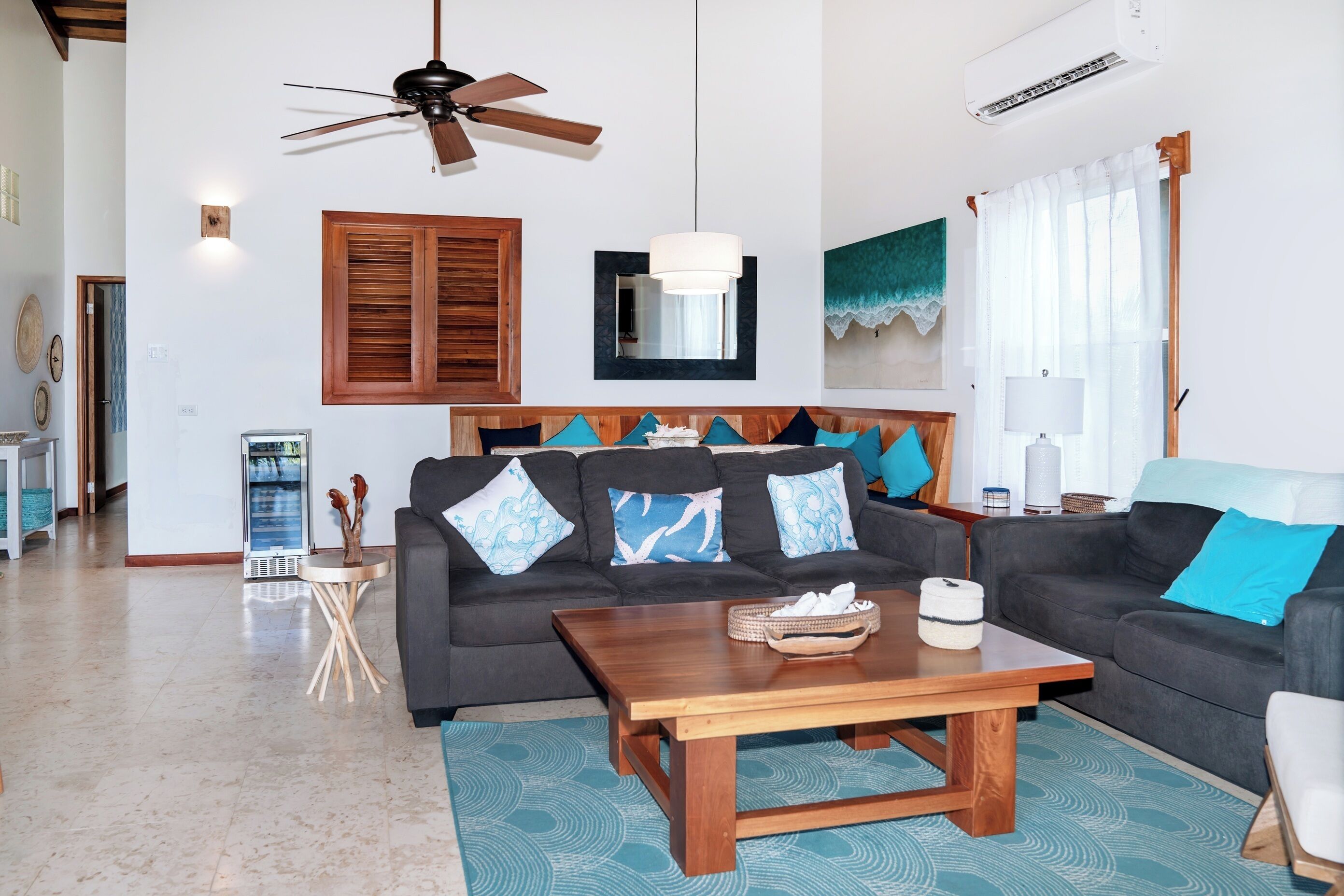 A living room with two sofas, a wooden coffee table, a ceiling fan, a large mirror, and a window with curtains.