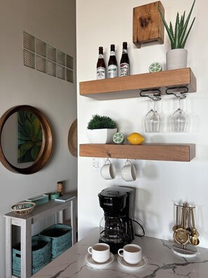 A kitchen with wooden shelves holding bottles, a coffee maker, and a potted plant. - Oceanfront 2BR Condo | Pools, Balcony + Reef Views (San Pedro Town)