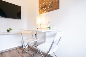 Ein modernes Zimmer mit Flachbildfernseher, Schreibtisch mit Lampe, zwei weißen Stühlen und einer Wanddekoration.