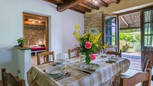 A dining area with a table set for four, a stone wall, and a view of the garden. - Appartamento rustico con piscina nell'antico "Podere la Querciola, Guardistallo" (Guardistallo)