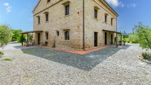 A stone building with a gravel courtyard, outdoor seating, and a clear sky. - Appartamento rustico con piscina nell'antico "Podere la Querciola, Guardistallo" (Guardistallo)