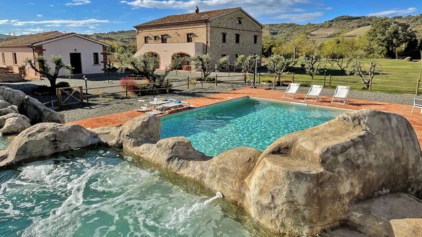 A pool with clear water, surrounded by large rocks, and a building in the background. - Appartamento rustico con piscina nell'antico "Podere la Querciola, Guardistallo" (Guardistallo)