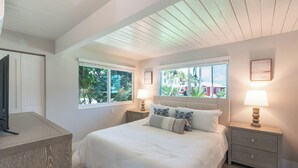 A bedroom with a large bed, two bedside tables, a nightstand, a TV, and windows with views of greenery. - ☀️Private Pool | Pet Friendly | Curlew Beach Cottage☀️ (Fort Myers Beach)