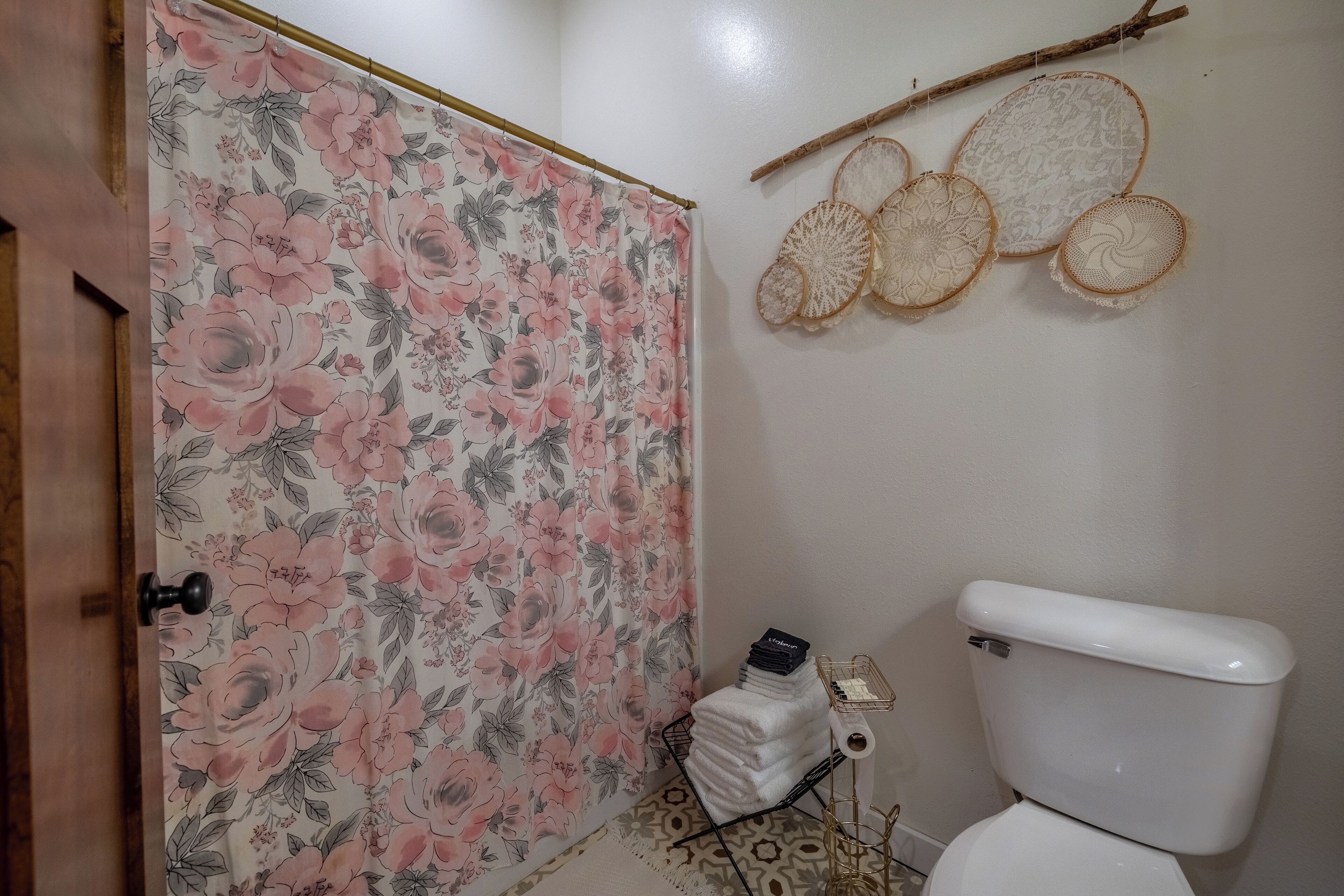Un baño con cortina de ducha estampada con flores, un inodoro y adornos en la pared.