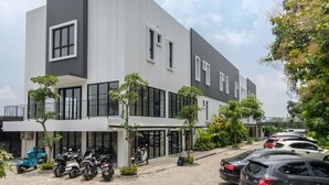 Un edificio moderno con techo plano, ventanas amplias y un balcón. Varias motocicletas y automóviles estacionados en la parte frontal.