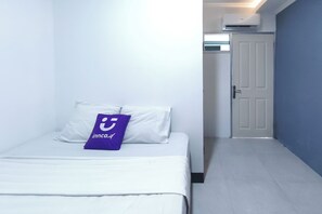 Quarto de hotel com uma cama, um travesseiro com logótipo, uma porta e um corredor.