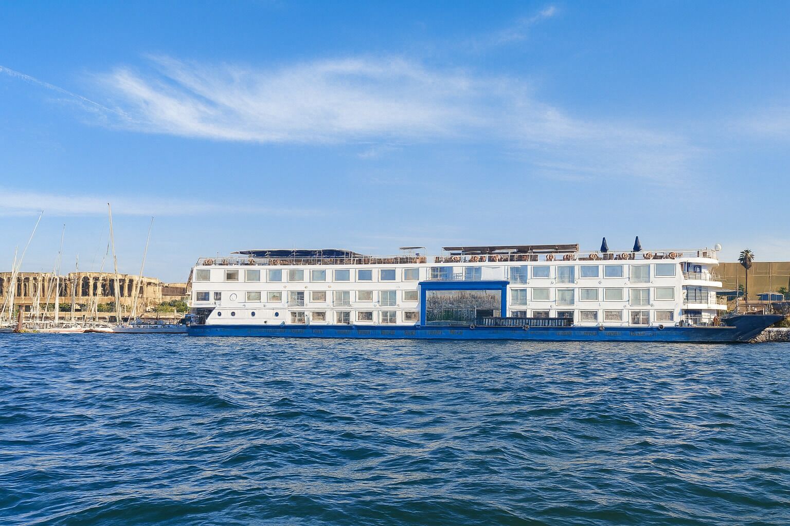 Ein großes, mehrstöckiges Flusskreuzfahrtschiff mit blau-weißer Farbgebung liegt an einem Steg, im Hintergrund ist ein klarer Himmel zu sehen.