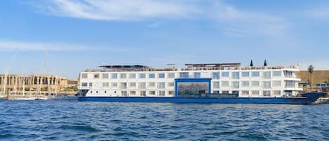 Ein großes, mehrstöckiges Flusskreuzfahrtschiff mit blau-weißer Farbgebung liegt an einem Steg, im Hintergrund ist ein klarer Himmel zu sehen.