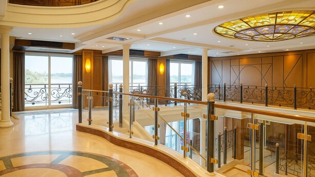 A spacious interior with a grand staircase, large windows offering a view, and ornate ceiling details. - Nile Cruise Suites Only every Friday from Aswan 3 nights & every Monday from Luxor 4 nights (Aswan)