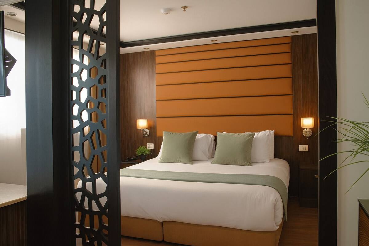 Una habitación de hotel con una cama, dos mesitas de noche, un cabecero de madera y un biombo decorativo.