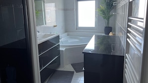 A modern bathroom with a bathtub, a large mirror, and a potted plant. - Chez Christophe Pauillac  (Pauillac)