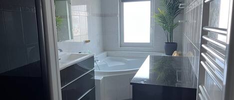 Un baño moderno con bañera, un espejo grande y una planta en maceta.